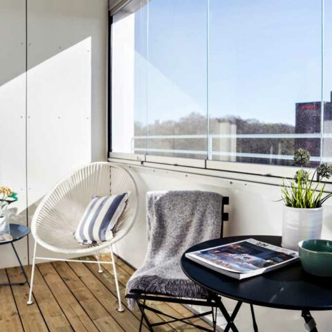 En inglasad balkong med ett litet svart bord och två stolar står på