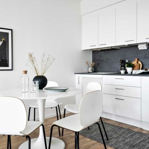 Ett kök och vardagsrum i öppen planlösning. Vita väggar, vitt kök och en beige soffa.