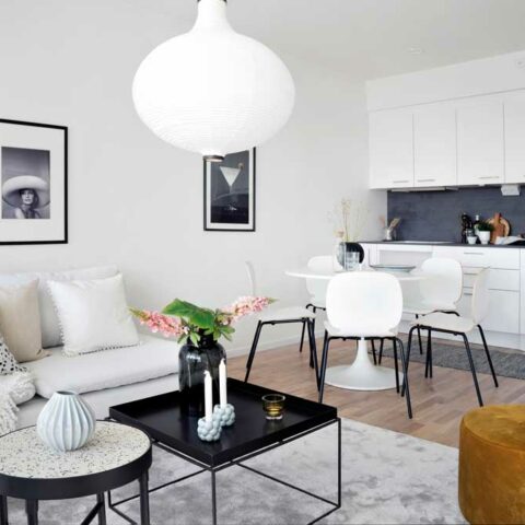 Ett kök och vardagsrum i öppen planlösning. Vita väggar, vitt kök och en beige soffa.