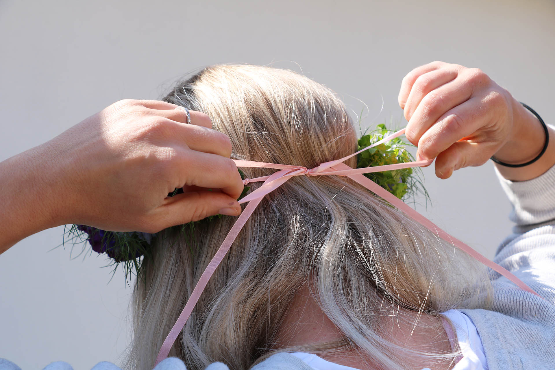 En tjej med blont hår sätter fast en midsommarkrans med ett rosa band runt hennes huvud