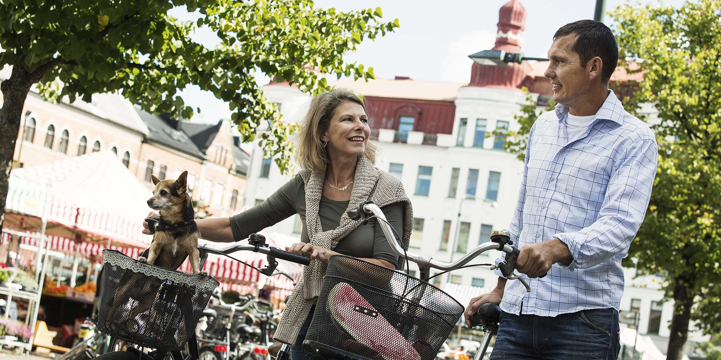 En kvinna och en man går och leder sina cyklar i en stadsmiljö
