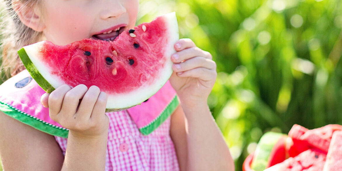 En närbild på en stor vattenmelon bit som en liten flicka äter på.