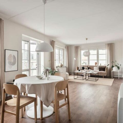 Öppen planlösning mellan vardagsrum och kök. Man ser en beige soffa i bakgrunden och ett köksbord närmast