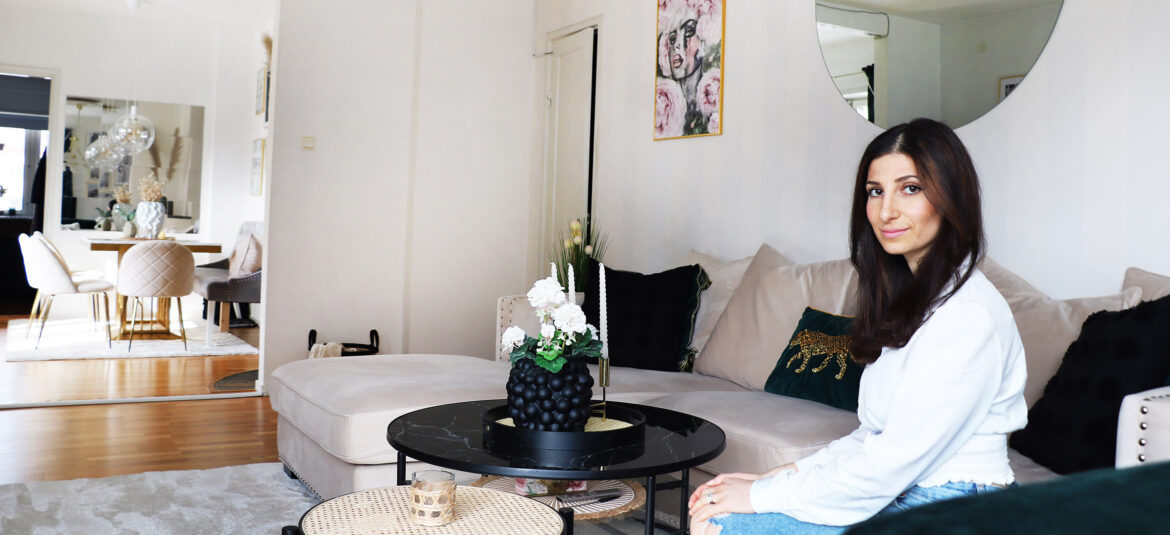 En tjej med mörkt långt hår sitter i en ljus beige soffa. Framför står det ett runt svart bord.