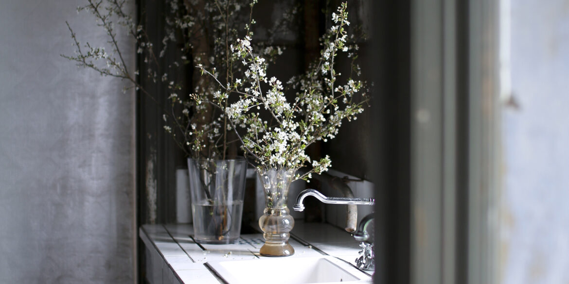 Ett mörkt kök där en vas med blommor står på en vit köksbänk
