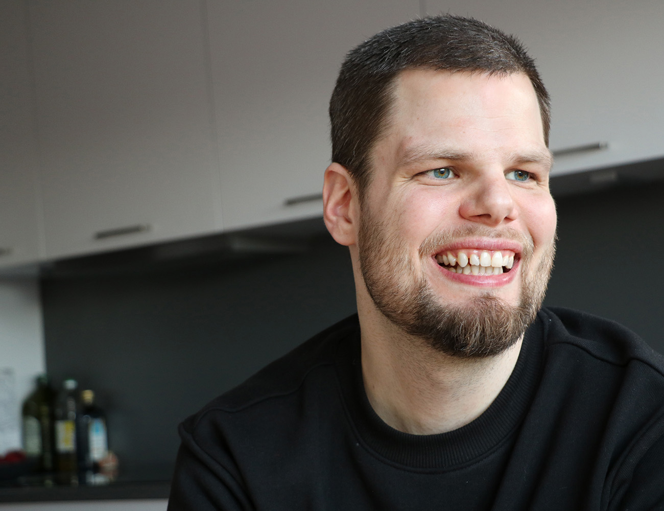 En man med kort mörkt hår och en svart tröja ler mot kameran