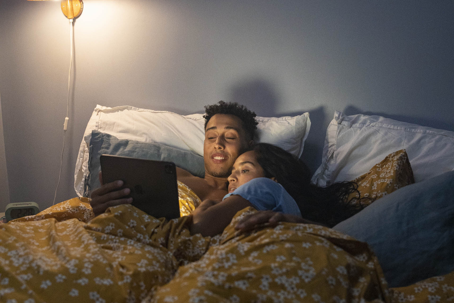 Ett par ligger i sängen under täcket och tittar på en iPad tillsammans