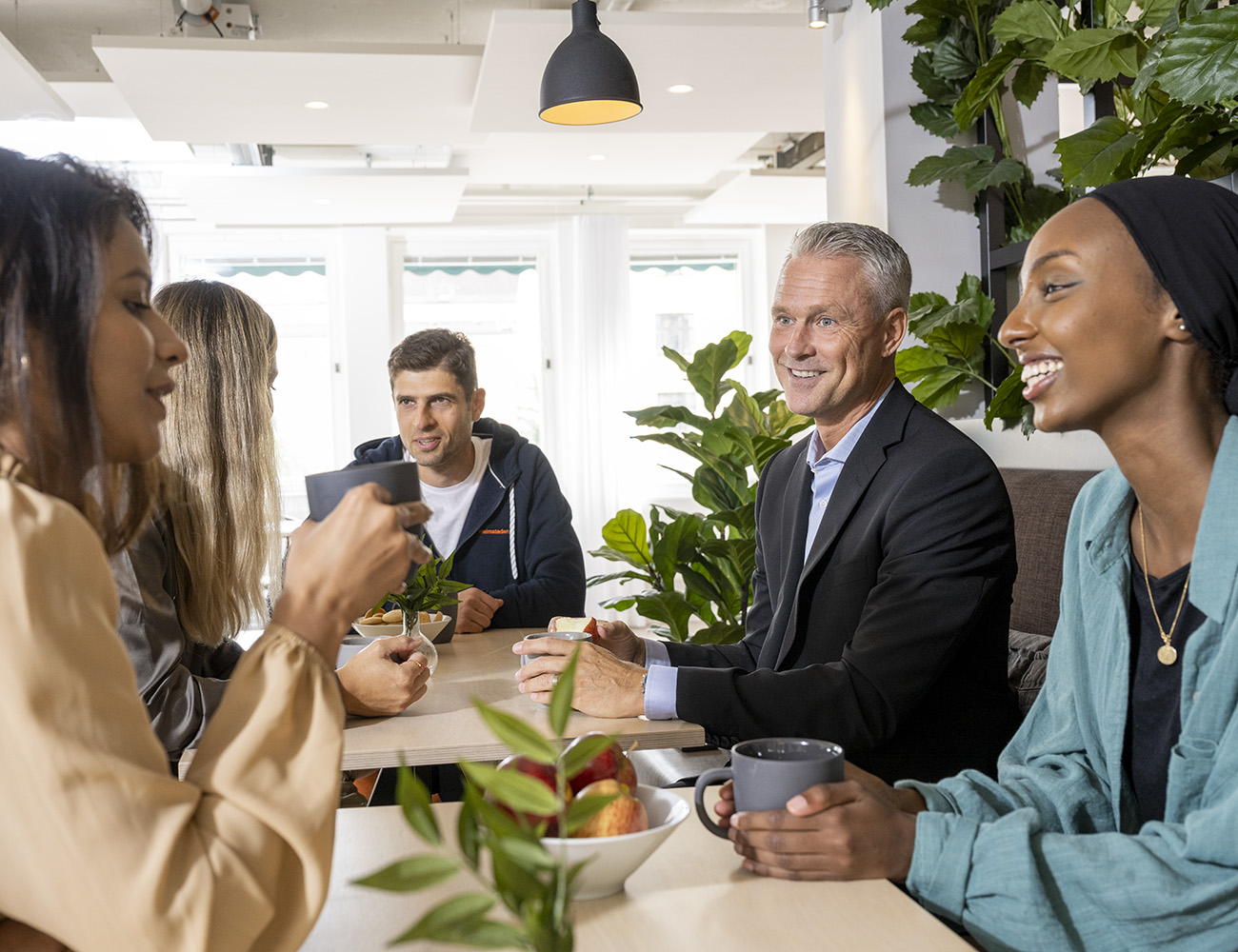 Några personer sitter runt ett bort på en arbetsplats och dricker kaffe och pratar.