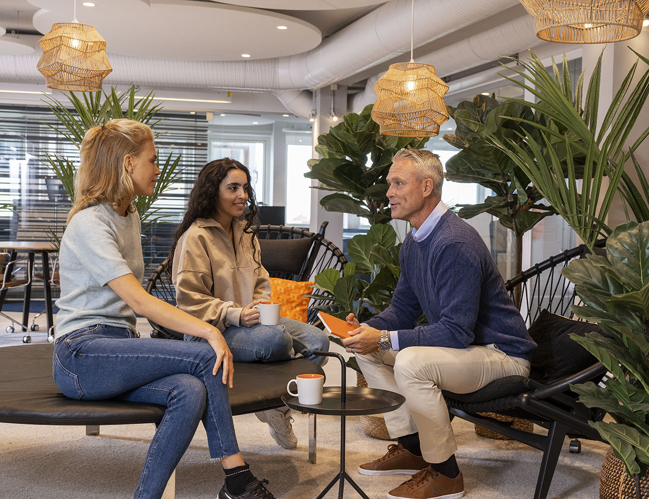 Två kvinnor och en man sitter i en soffgrupp på en arbetsplats och pratar.