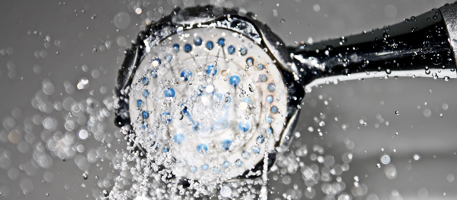 En närbild på ett duschmunstycke som det sprutar vatten ifrån.