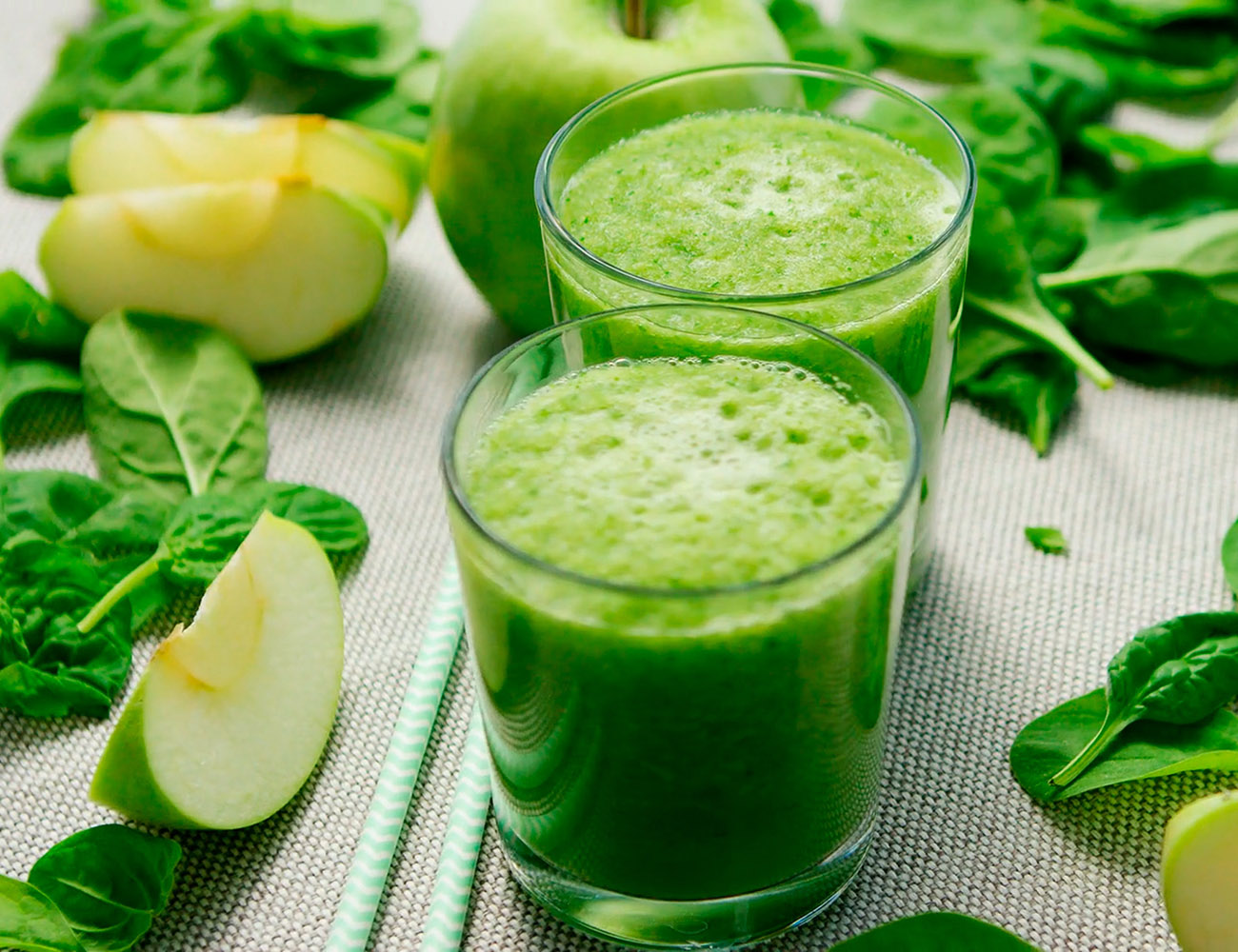 Ett glas med en grön smoothie med äppelskivor och spenat runt om.