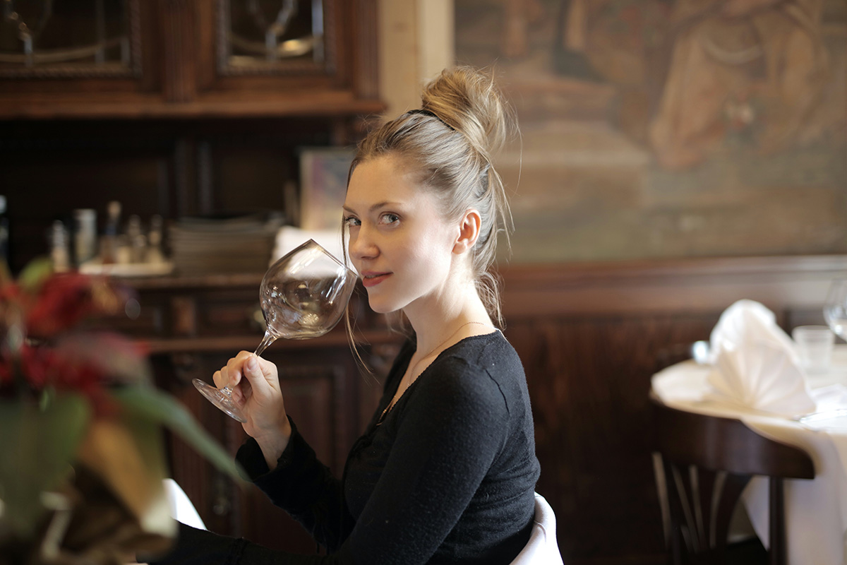 En kvinna med svart topp sitter med ett stort glas och dricker i en restaurang.