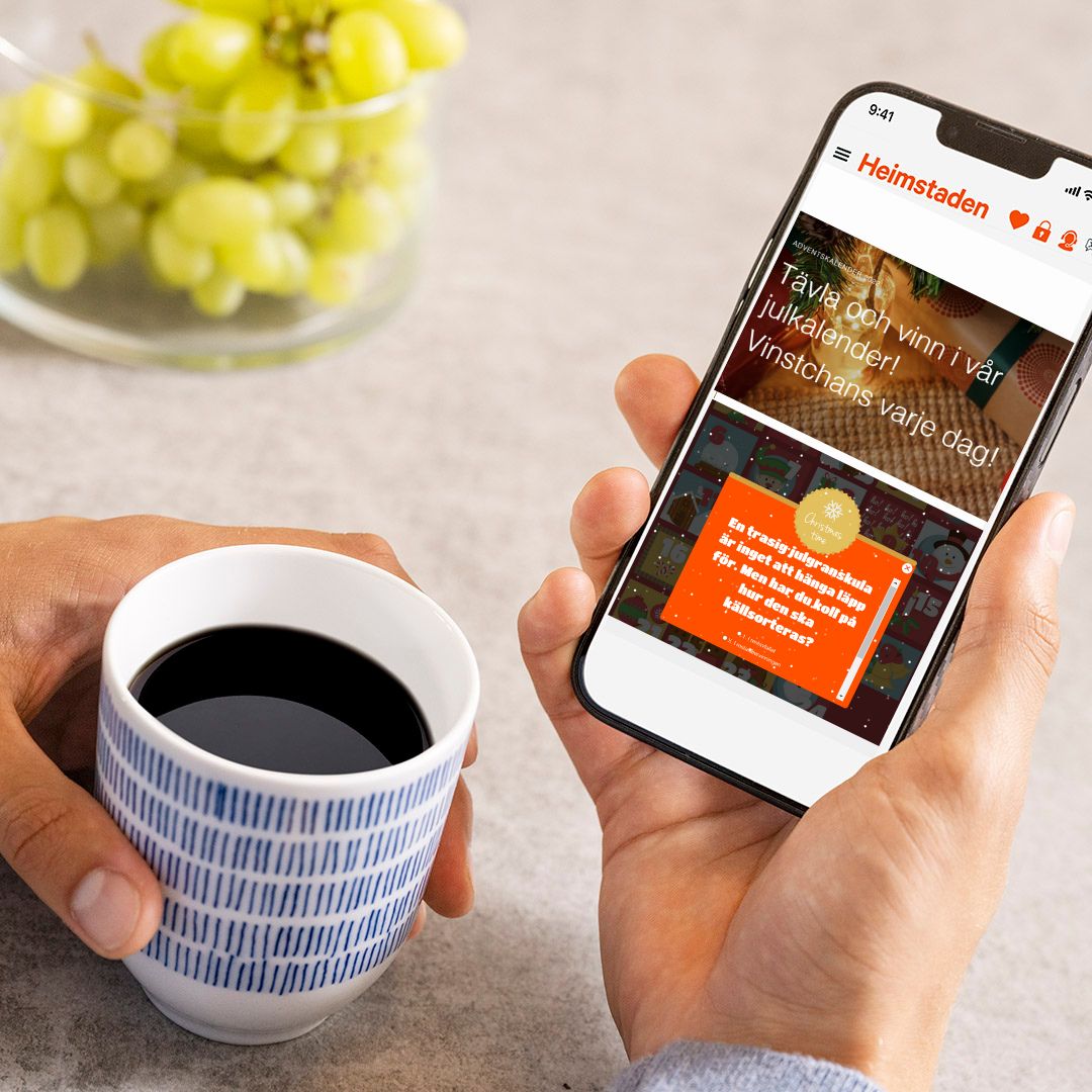 En närbild på en hand som håller i en mobil. I den andre handen håller hen en kaffekopp.