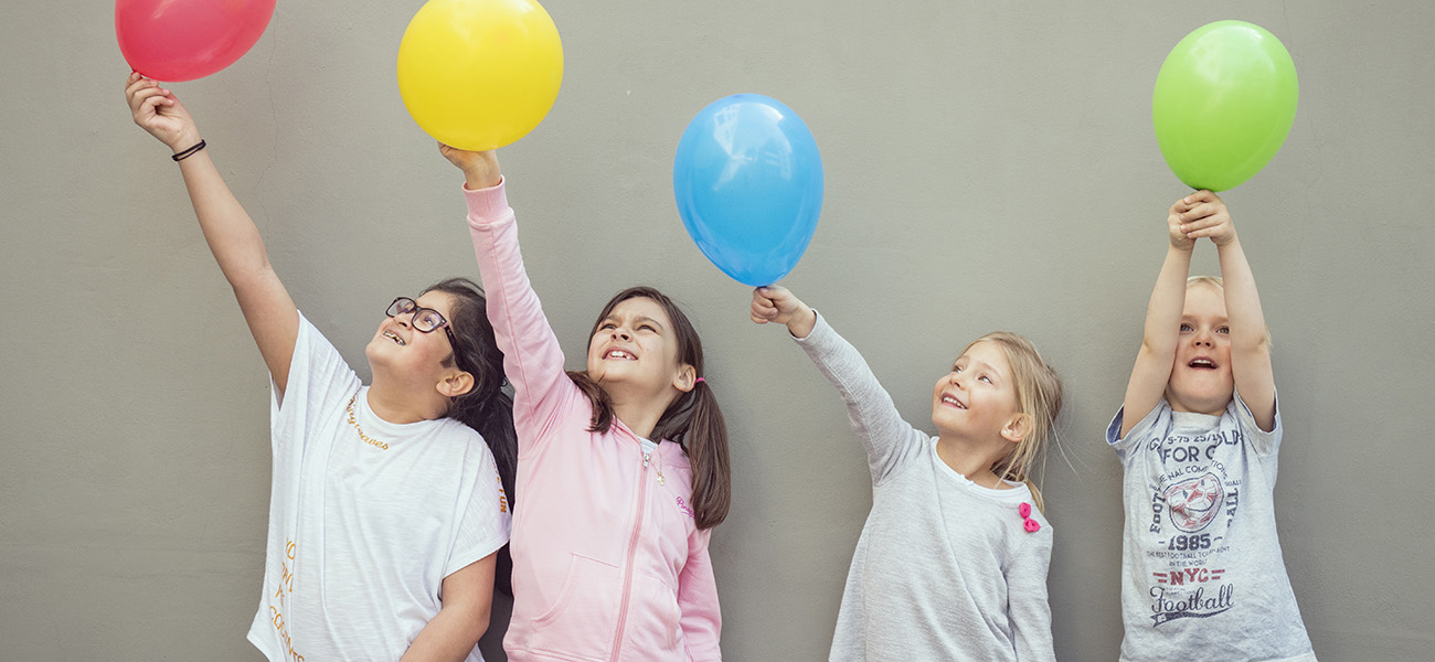Fyra barn står mot en grå vägg med en ballong i handen