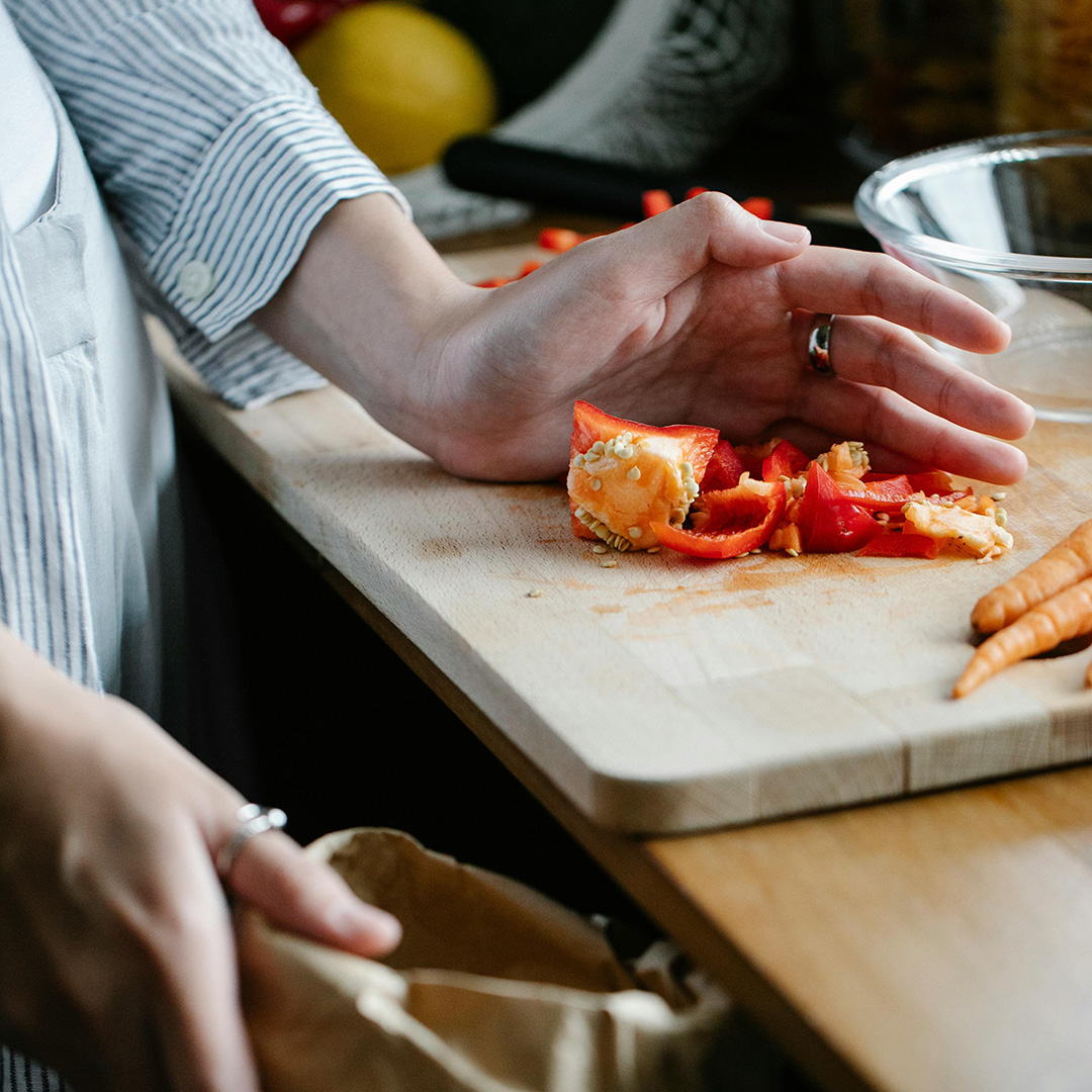 En närbild på en hand som föser ner paprika i en brun matpåse från en träskärbräda.
