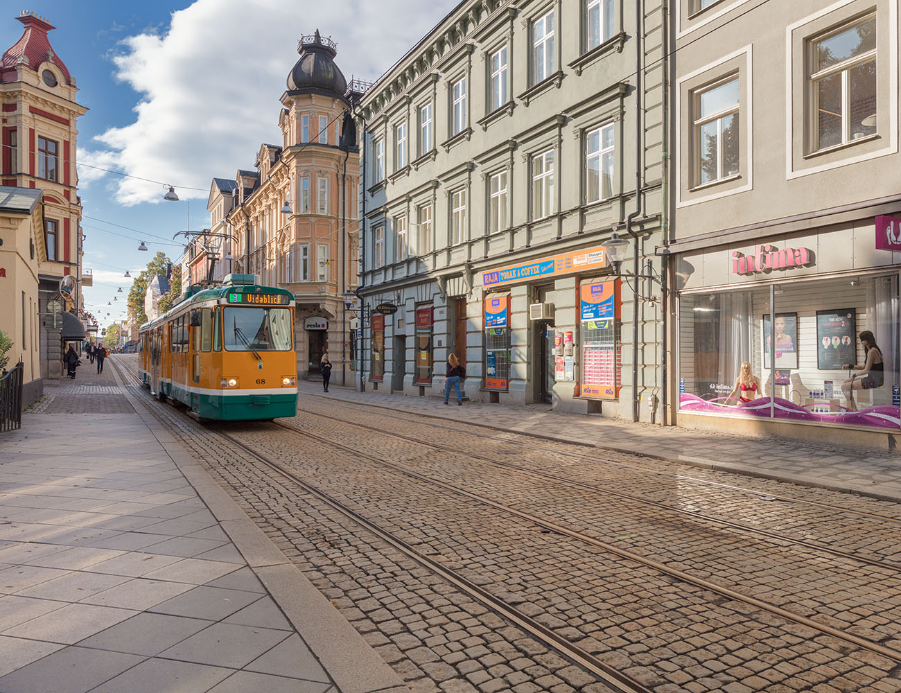 En stadsgata där man ser gamla sekelskifteshus och en gul spårvagn som kommer körandes.