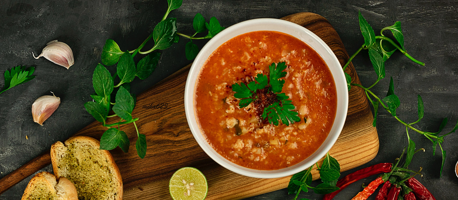 En vit tallrik med en röd tomatsoppa i. Den står på en träskärbräda och en bit lime ligger bredvid.
