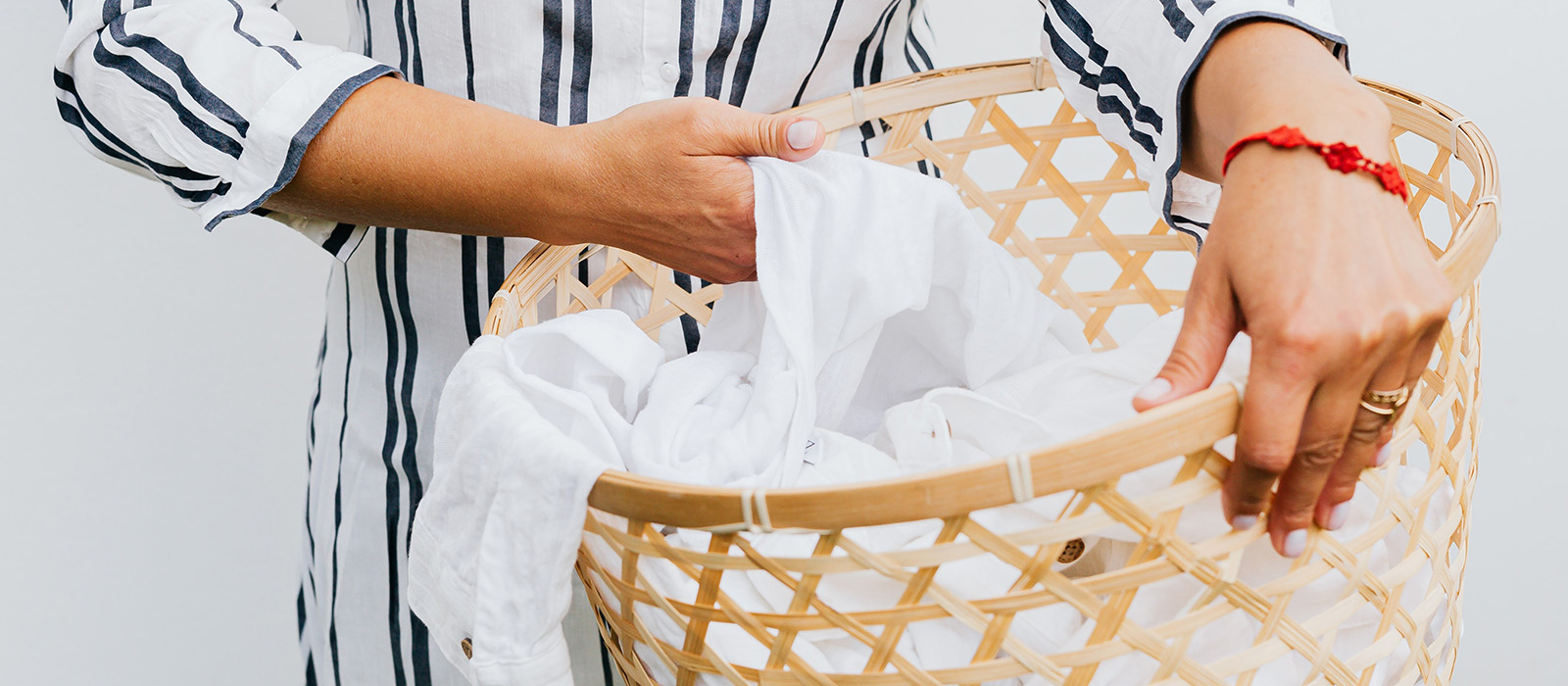 En närbild på en tvättkorg i ljus rotting. En kvinna i en randig skjorta lyfter upp en vit skjorta i korgen.