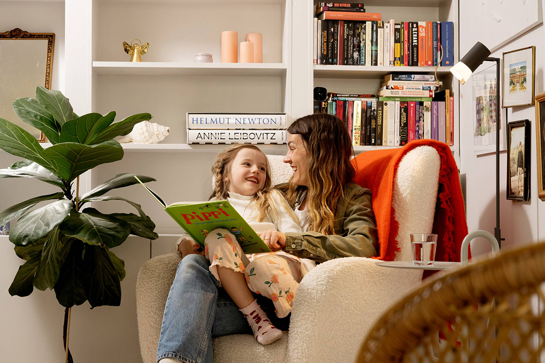 Mamma och dotter sitter i en fåtölj och läser tillsammans.