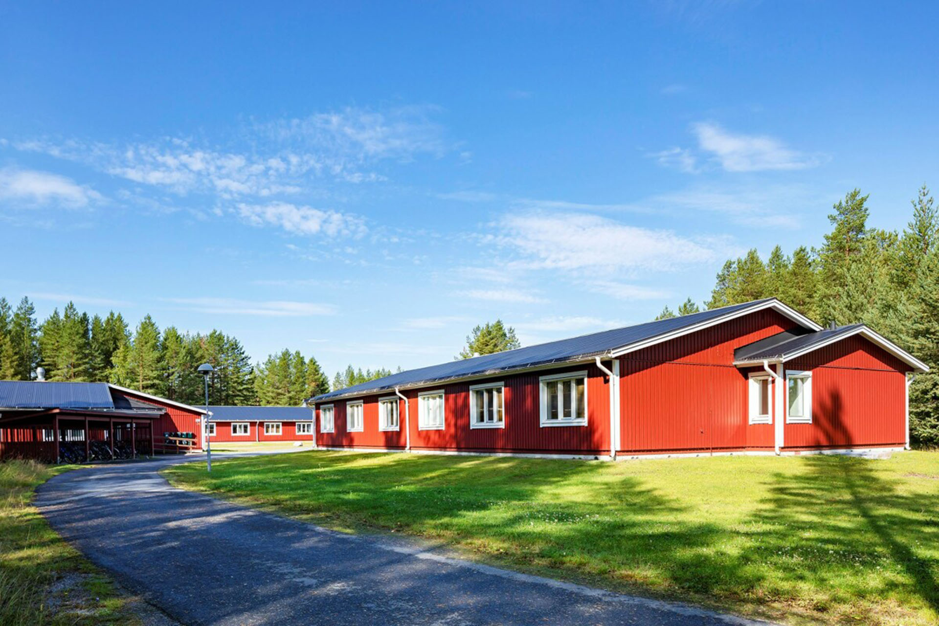 En låg röd träbyggnad med grönt gräs där Heimstaden erbjuder studentbostäder som man kan hyra,