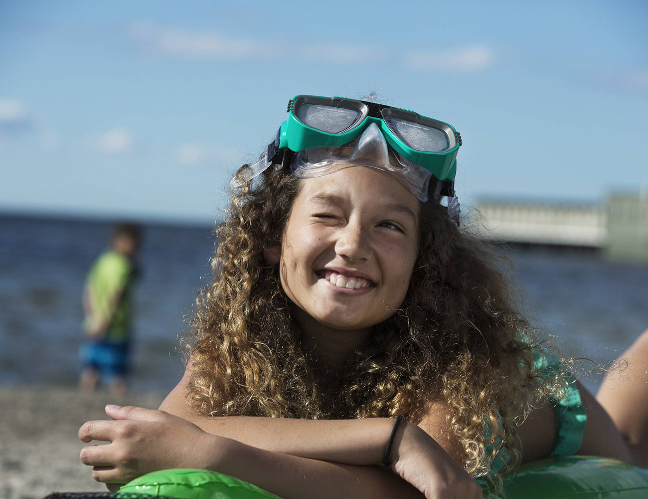 En ung flicka med mörkt lockigt hår och gröna simglasögon på huvudet.