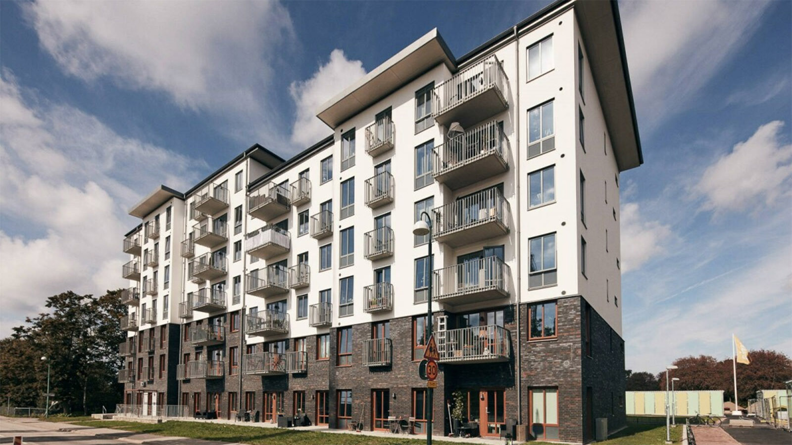 En vit bostadshusfasad med små balkonger på. Himlen är mörk och en känsla av åskoväder.