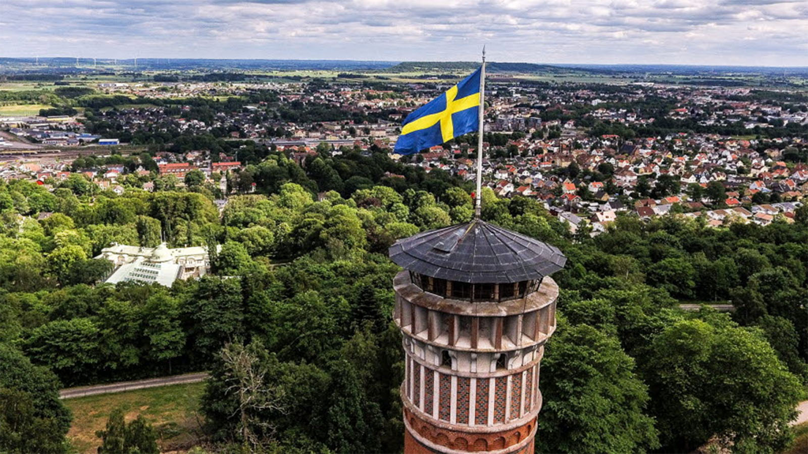 Ett högt torn med svenska flaggan på toppen och bakom ser man en stadsvy med massa villor och skogar.