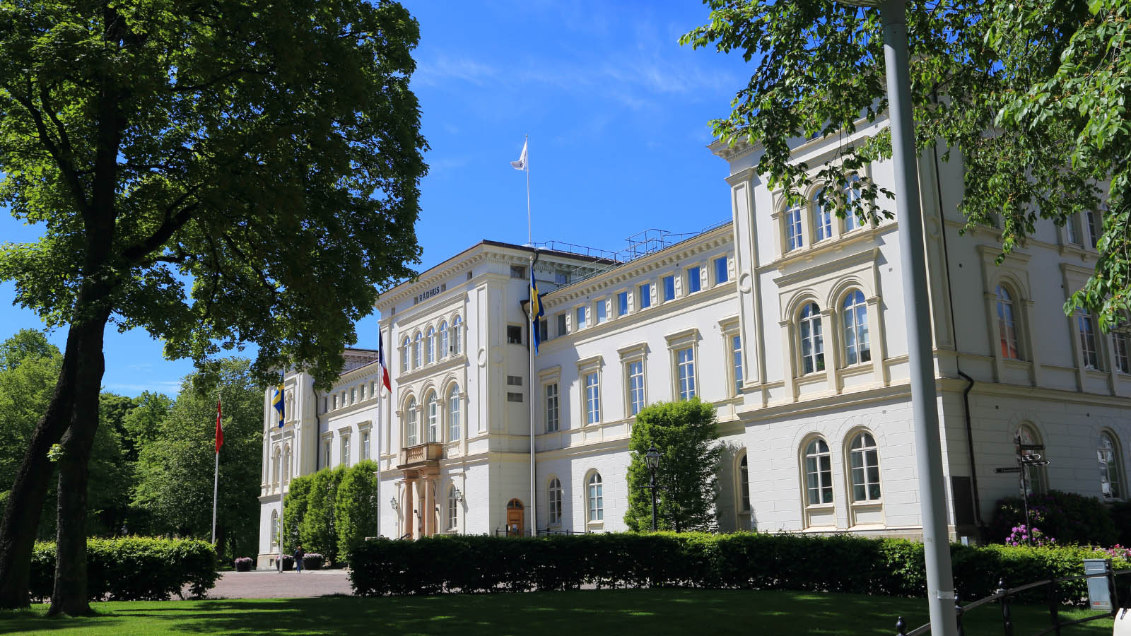 En gråvit gammal byggnad med stora gröna träd framför.