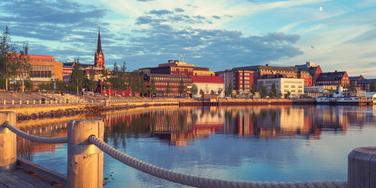 En stadsvy i skymningen över Luleå. Fasaderna speglar sig i vattnet.