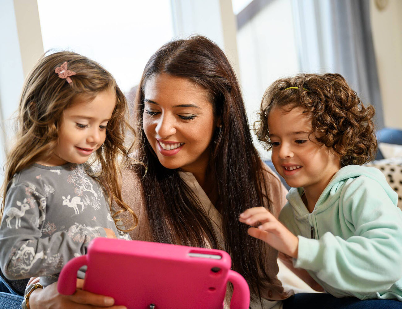 En mamma och två barn sitter tillsammans i ett tryggt hem och tittar på en iPad.
