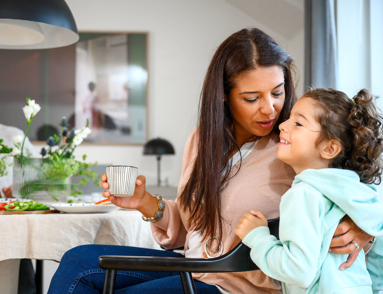 En mamma och dotter sitter i ett tryggt hem och kramas i soffan.