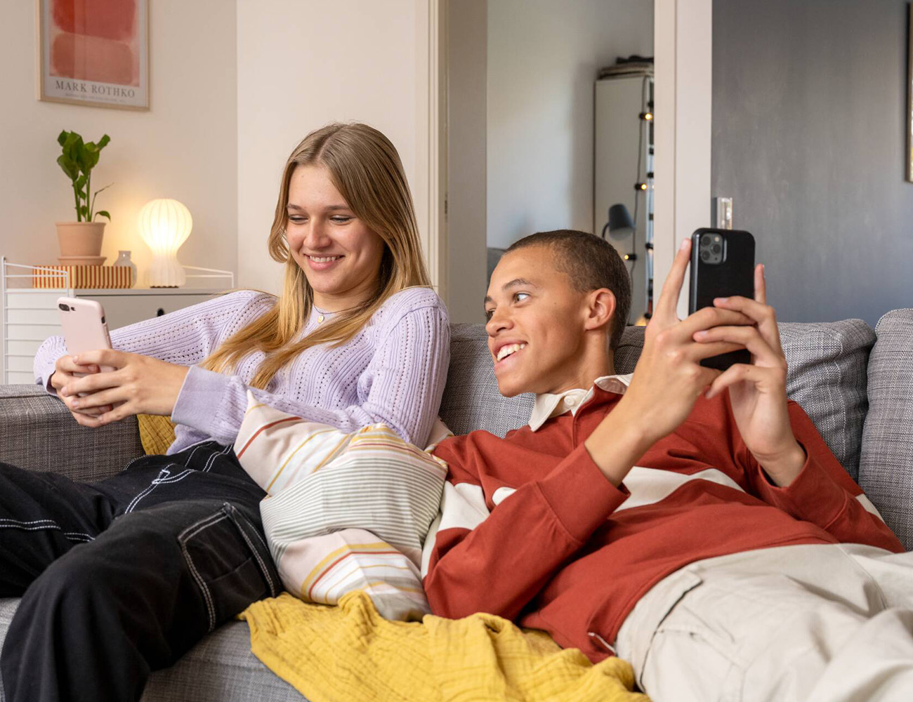 En tjej och kille sitter i en soffa och har varsin mobil i handen.