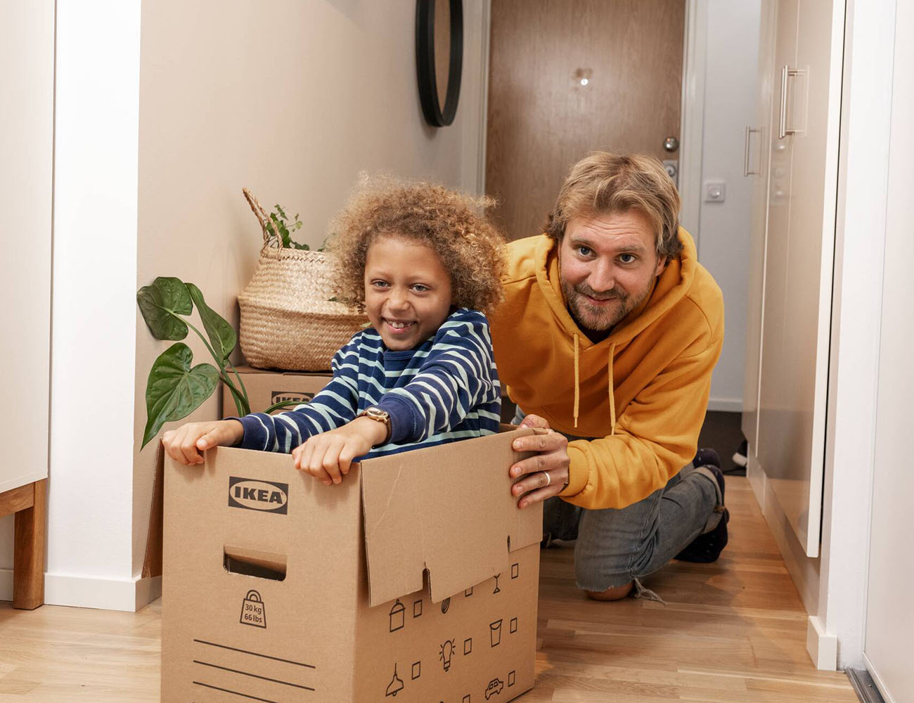 En man och ett barn som sitter i en flyttlåda ser glada ut för de har flyttat in i en ny lägenhet.