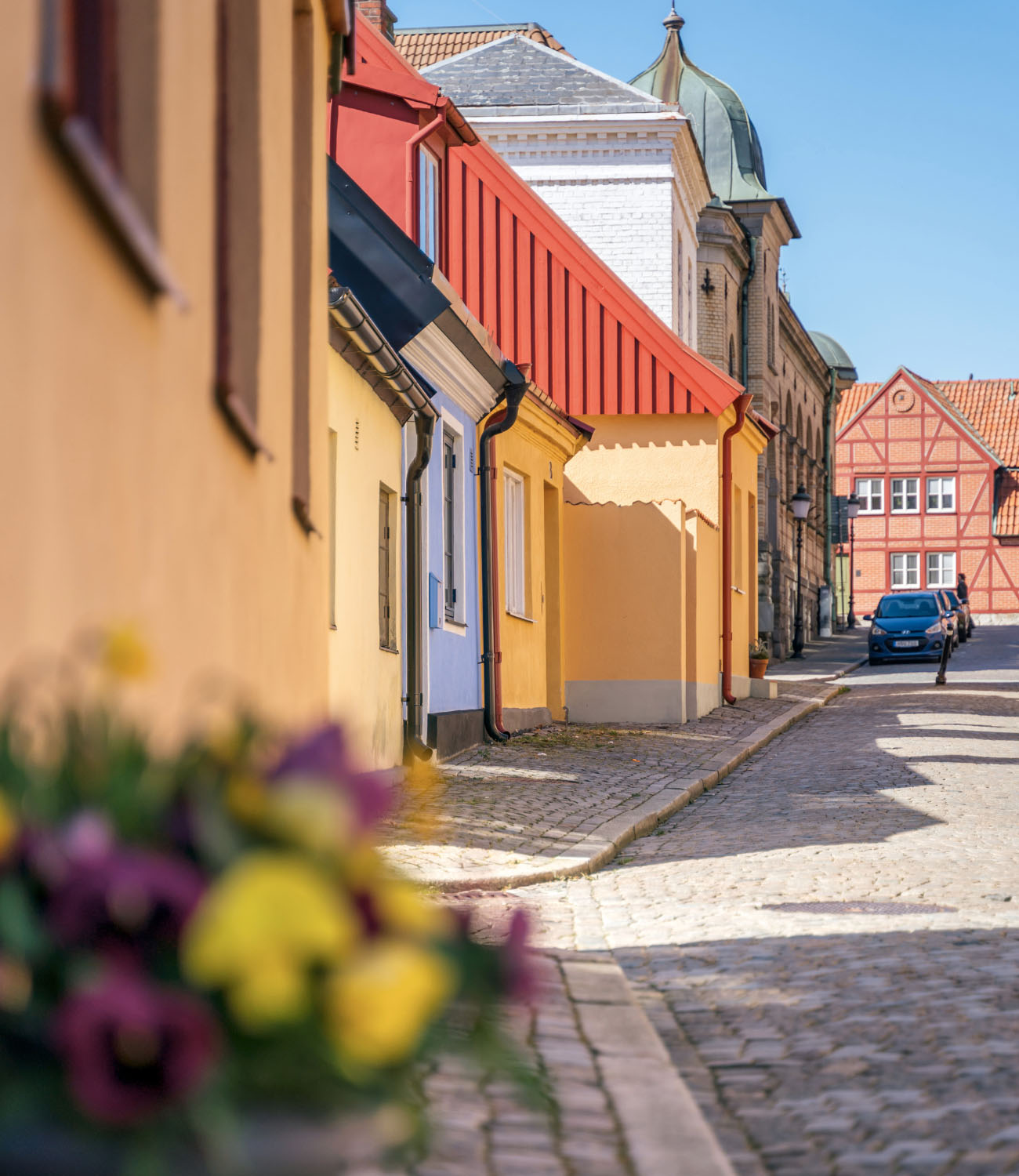En kullerstensgata i Ystad en sommardag med färgglada gatuhus.