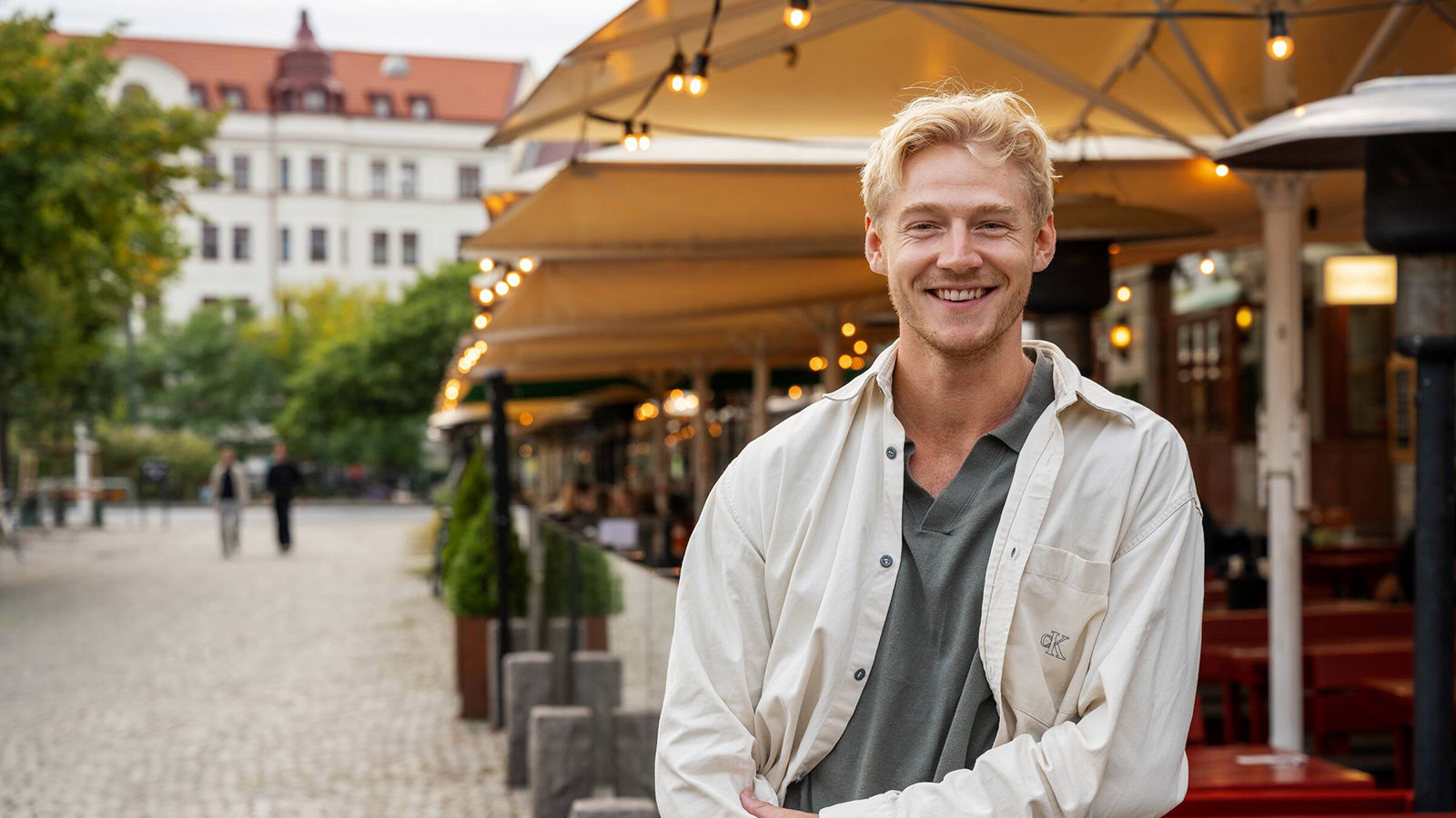 En ung kille står på Möllevångstorget i Malmö framför uteserveringarna.