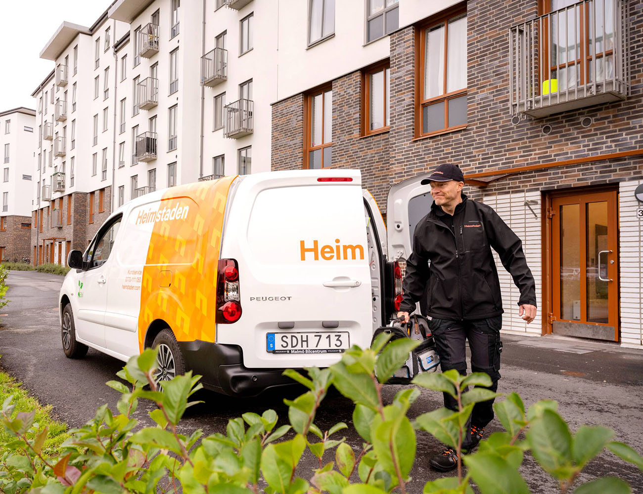 En vaktmästare på Heimstaden går utanför sin bil med en verktygslåda i handen och ska åtgärda ett fel i en bostad.