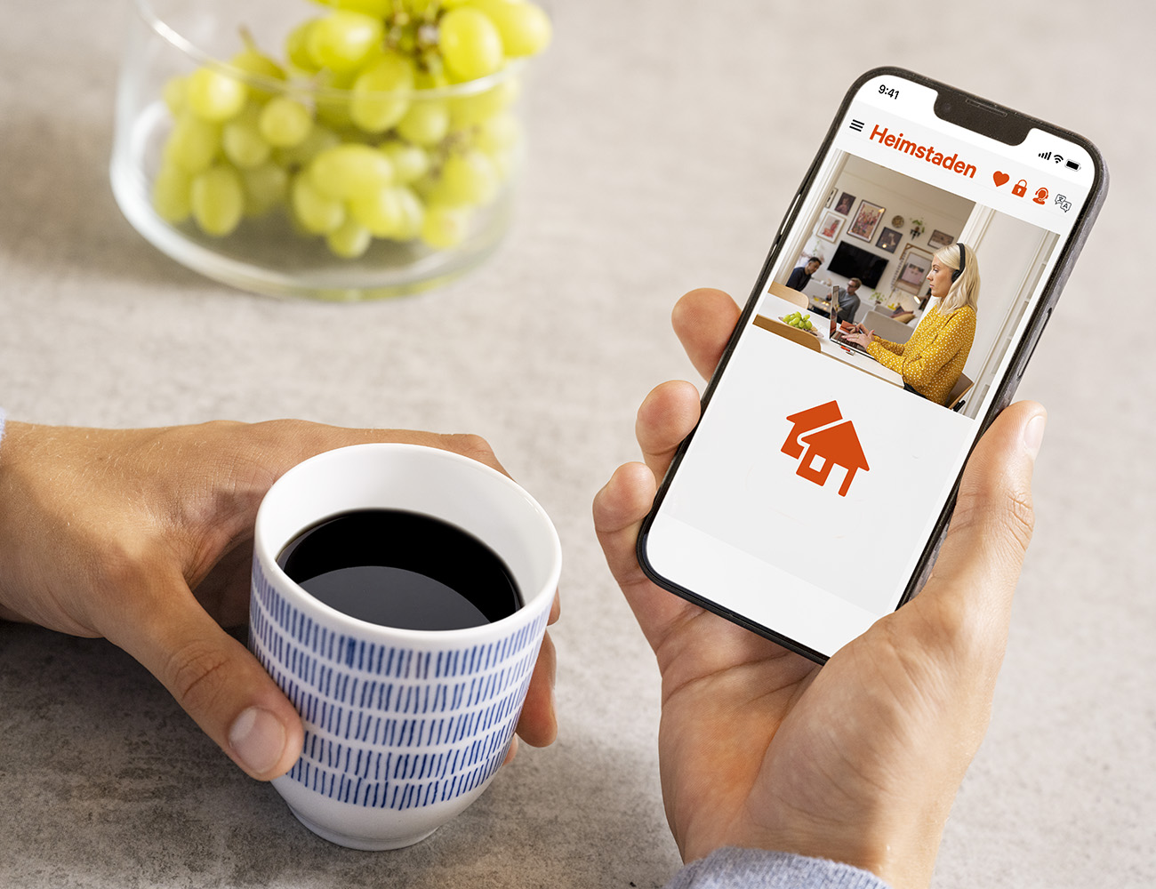 Närbild på två händer som håller en kaffekopp och en mobil som ska kolla in Heimstadens vanliga frågor och svar.