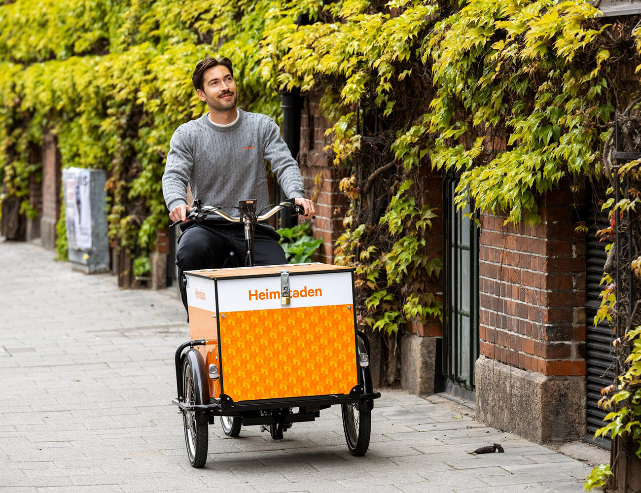 En kille cyklar på en Heimstaden lådcykel på en trottoar i Malmö.