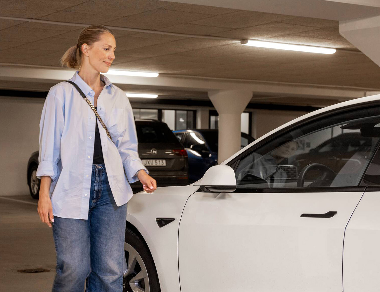 En kvinna med blå skjorta går fram till en vit parkerad bil i Heimstadens garage.