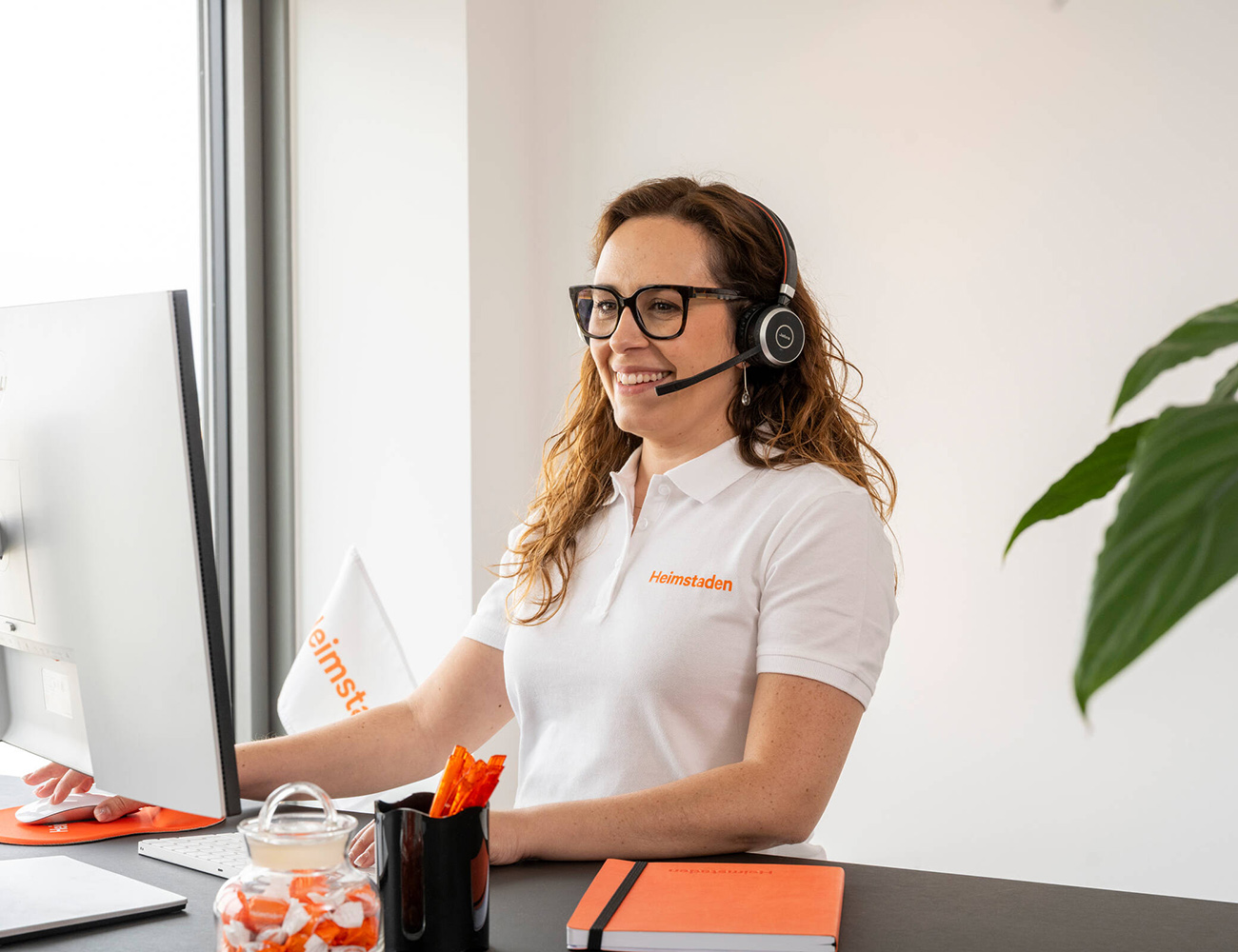 En anställd på Heimstaden pratar i sitt headset och tittar på datorn.