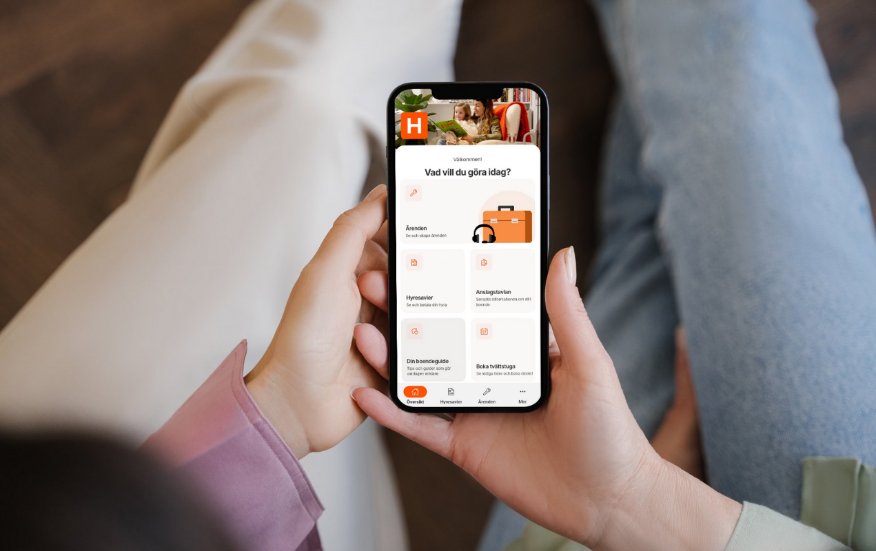 Två hyresgäster har en mobil i handen och kollar hur man loggar in i Heimstadens boendeapp.