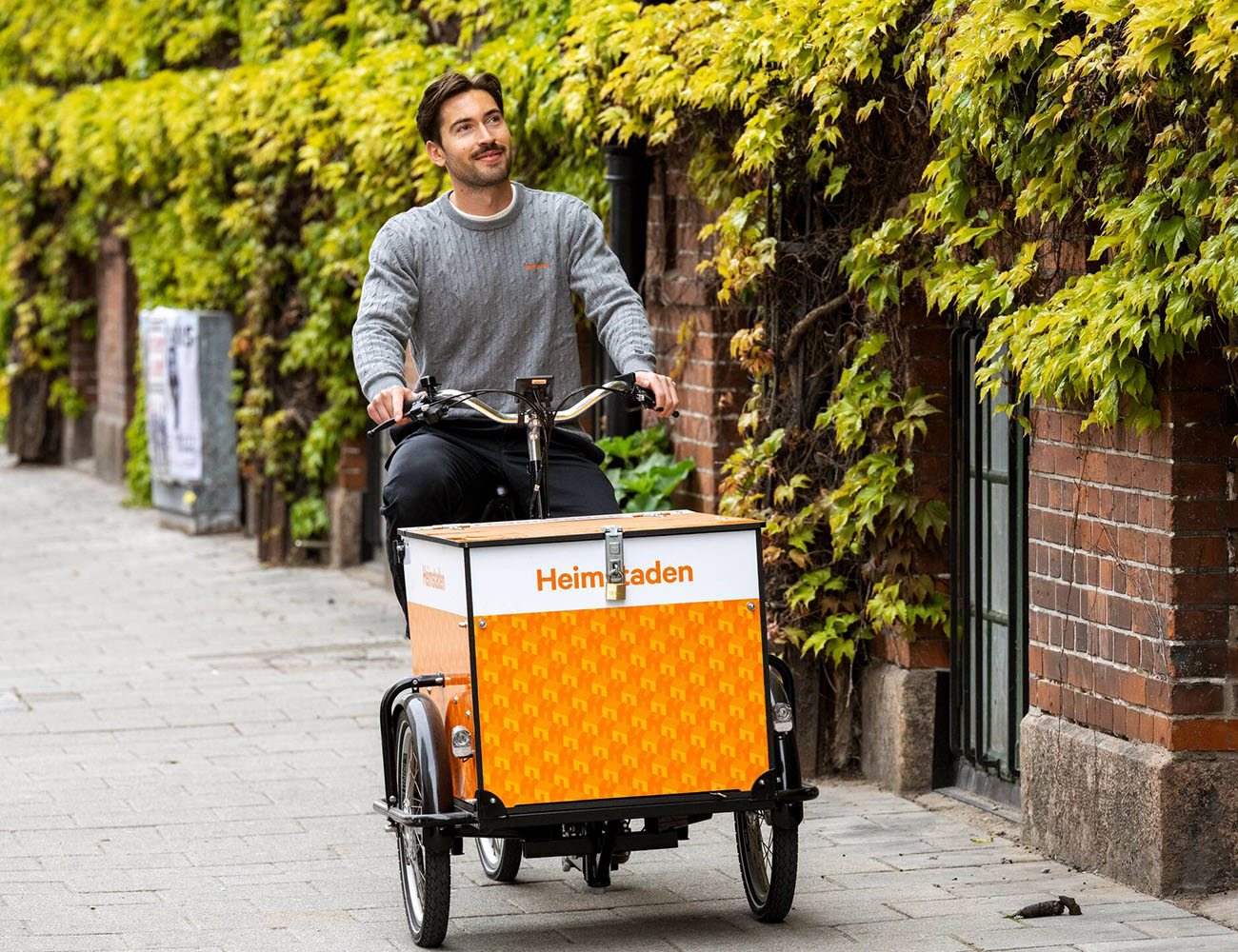 En kille cyklar på en Heimstaden lådcykel på en trottoar i Malmö där han hyr en lokal.
