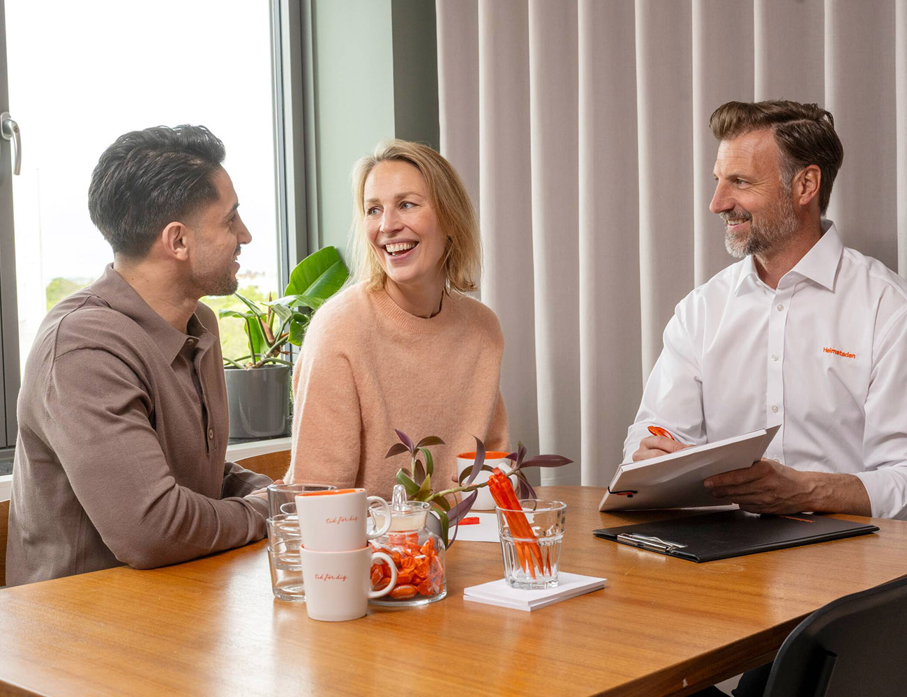 Ett par sitter vid skrivbordet med en uthyrare och ska skriva kontrakt för att flytta in i en Heimstaden hyrelägenhet.