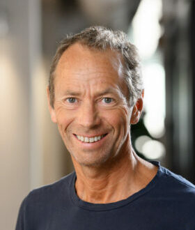 A man with short dark hair and a gray shirt smiles at the camera