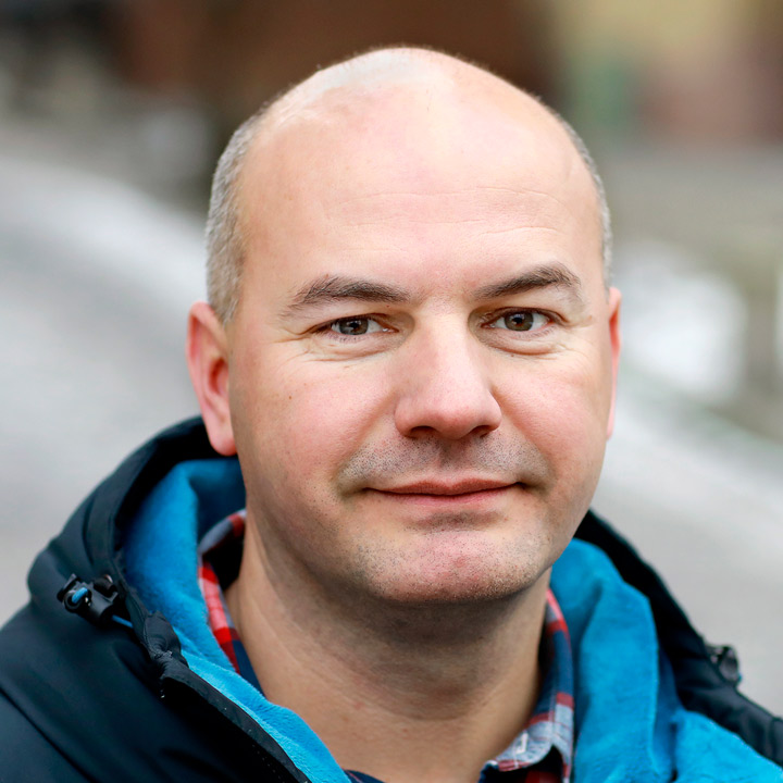 The face of a bald man with a black and blue jacket.