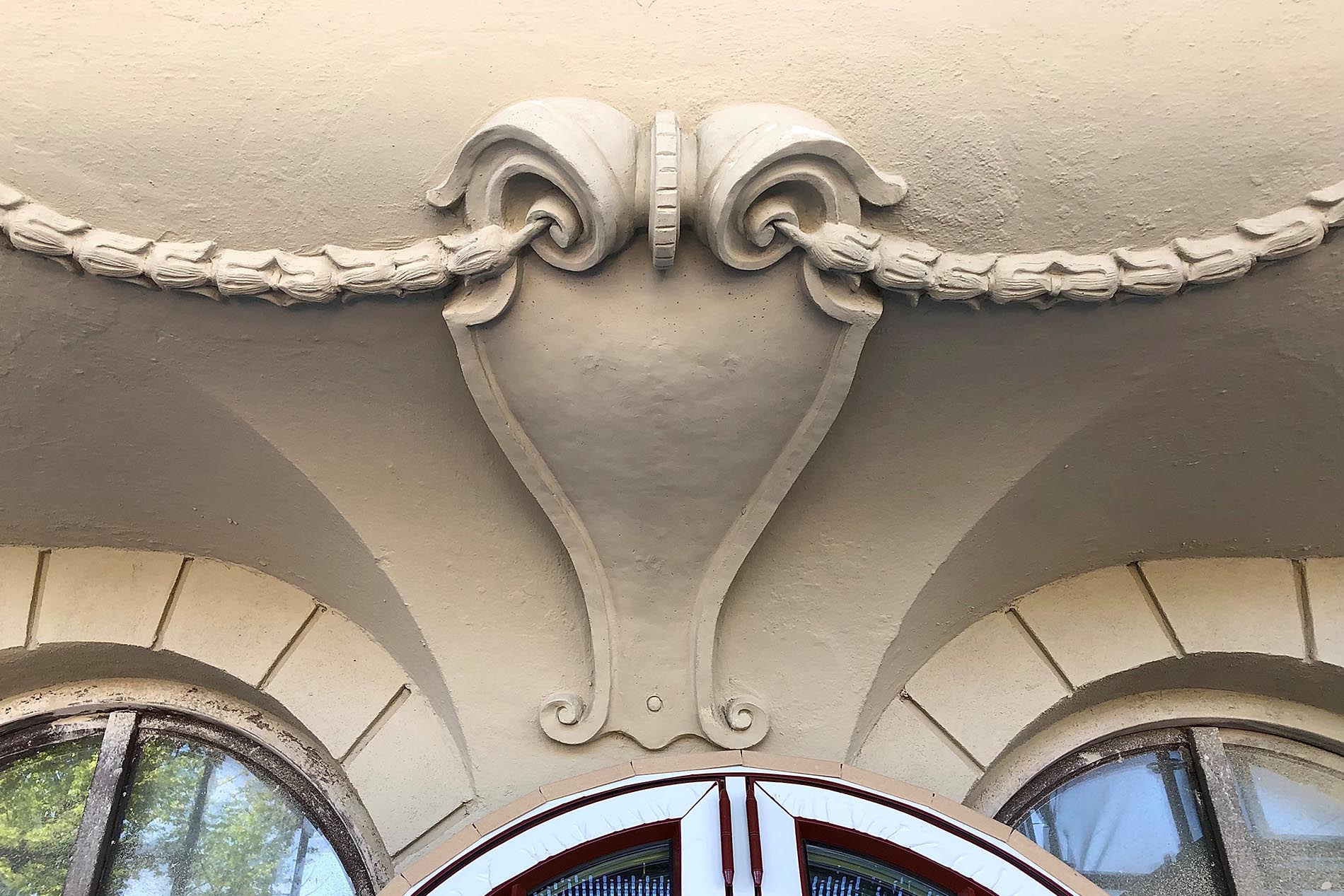 A decorative detail of a buildning, above the windows, in a plaster-coloured design