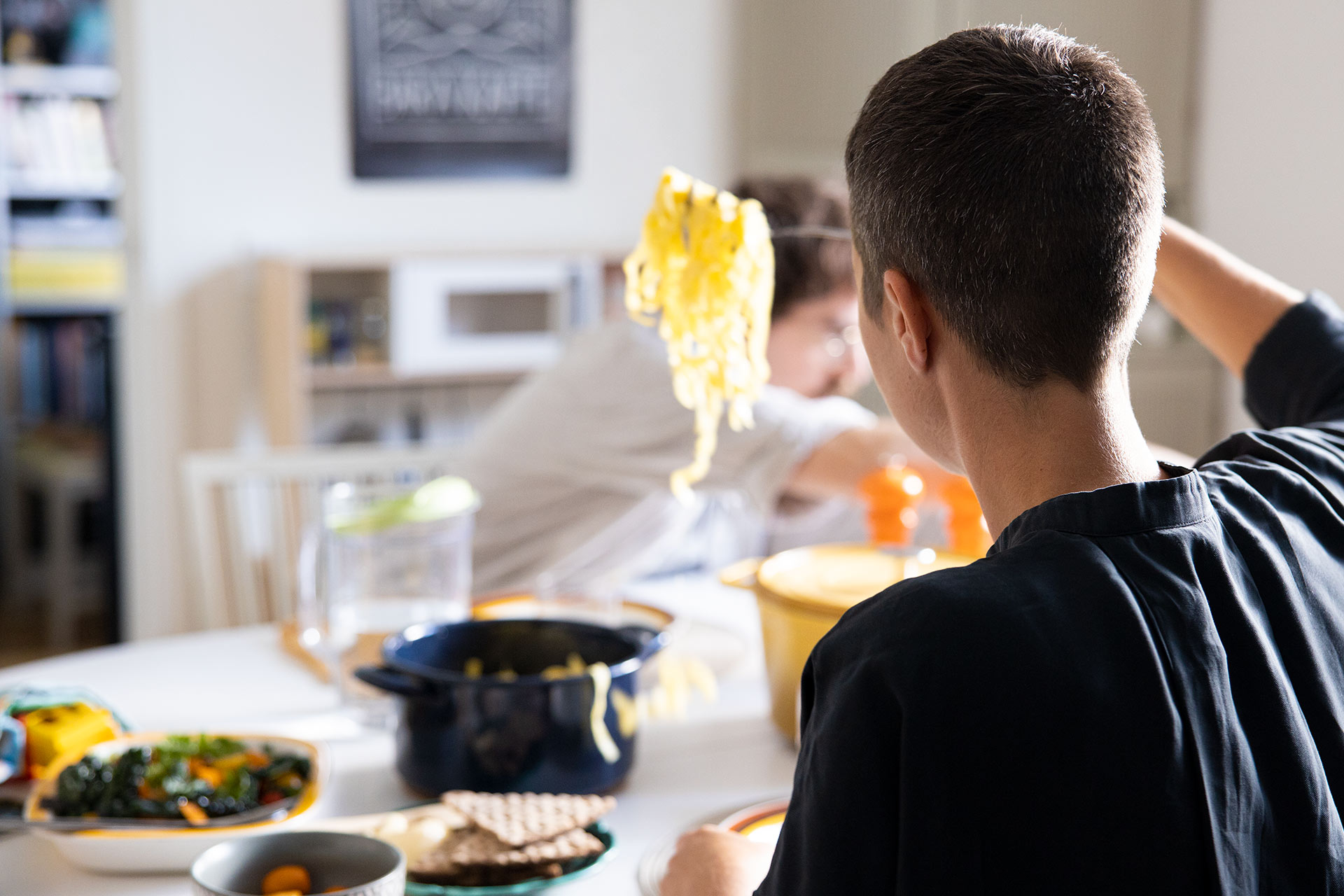 A woman at a table is taking spaghetti from a pot and putting it on her plate.