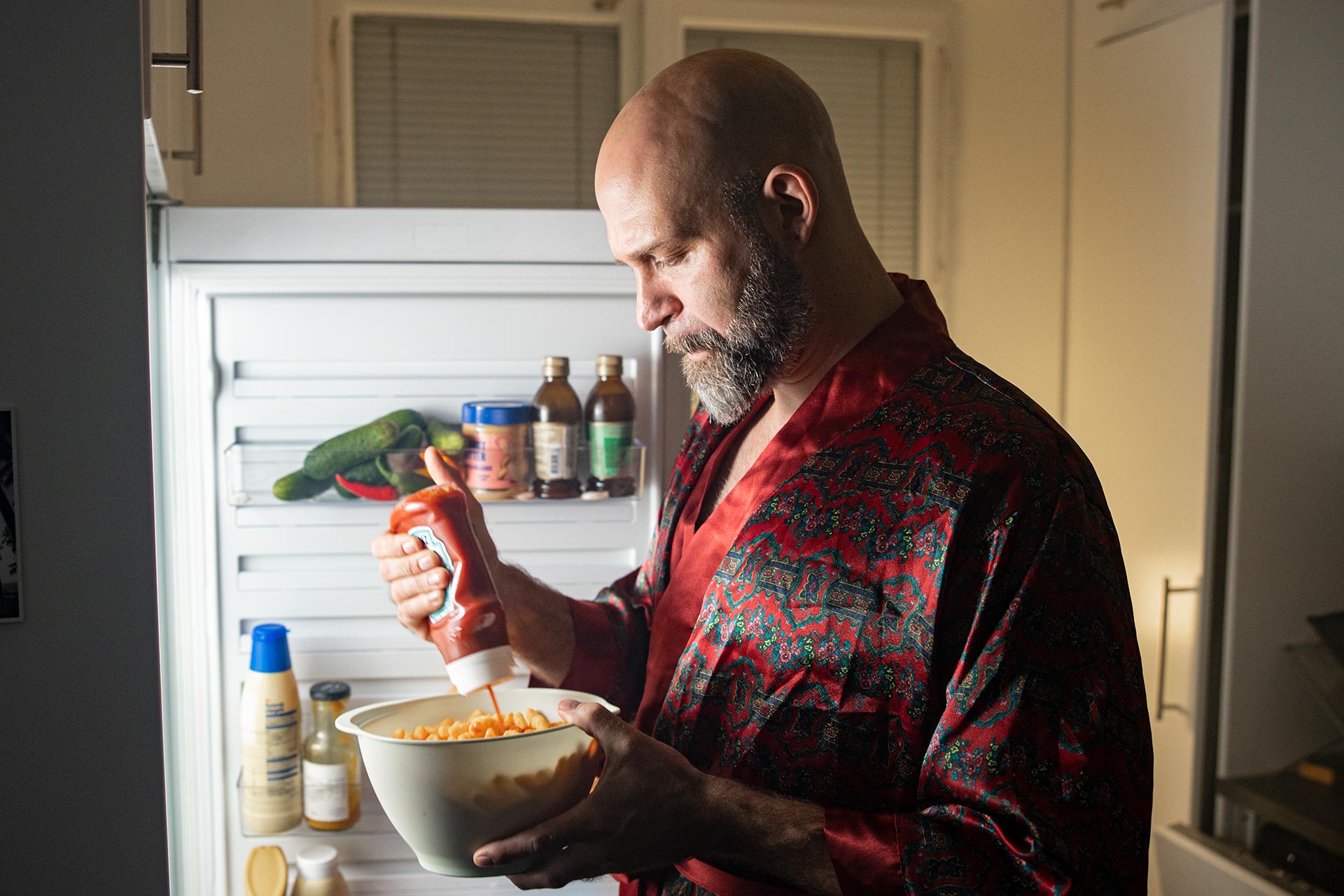 A man is eating food from a bowl directly from the fridge.