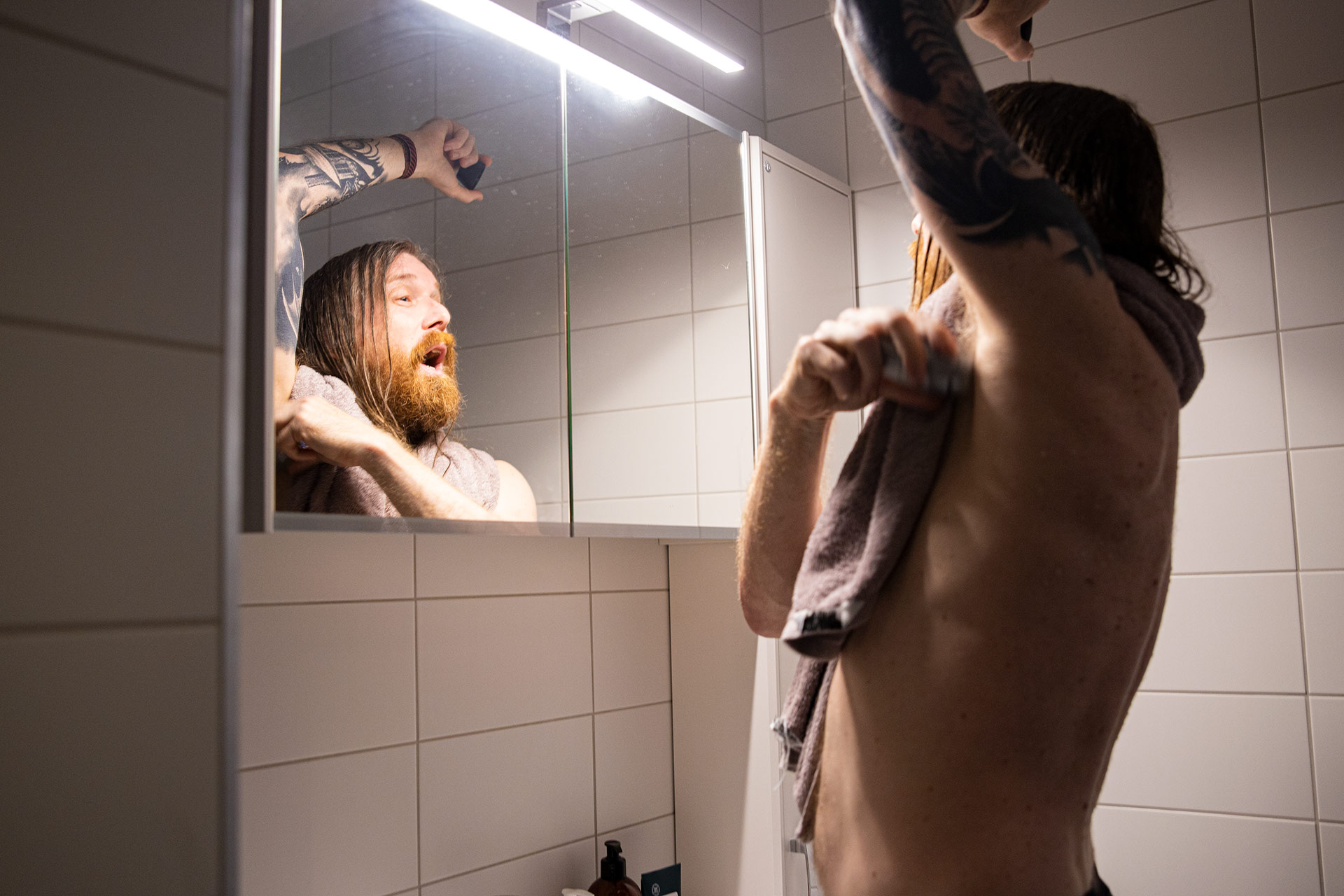 A man is applying deodorant in the bathroom in front of a mirror.