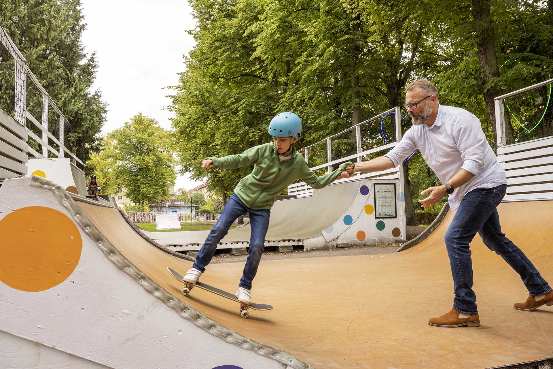 A man helps a boy skateboard in an outdoor ramp